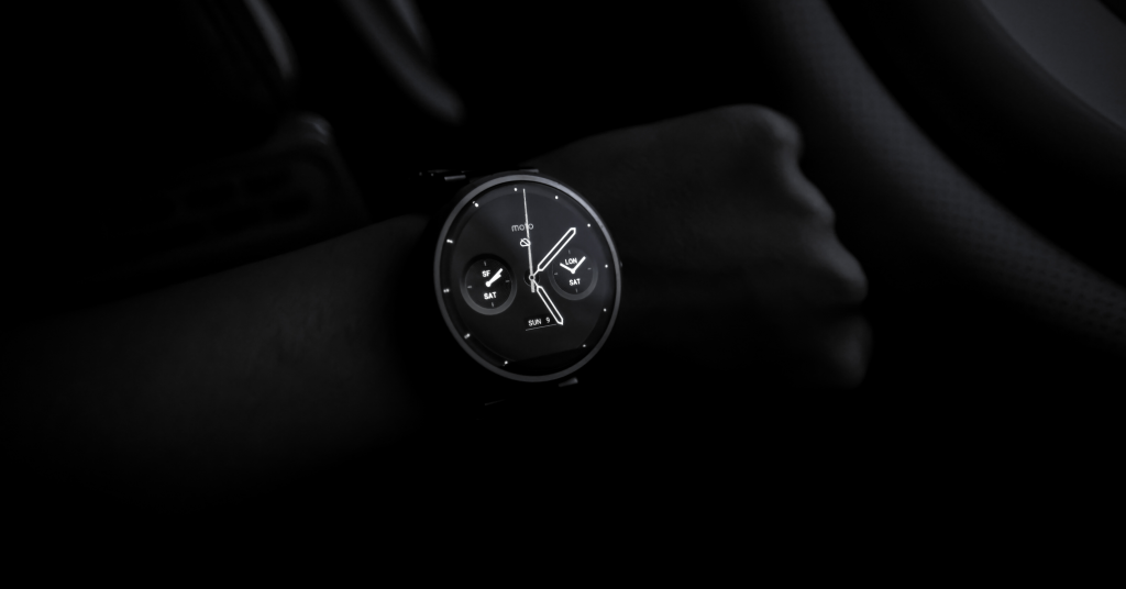 Black leather watch with a Black face and black hands, sitting on a black wool surface.