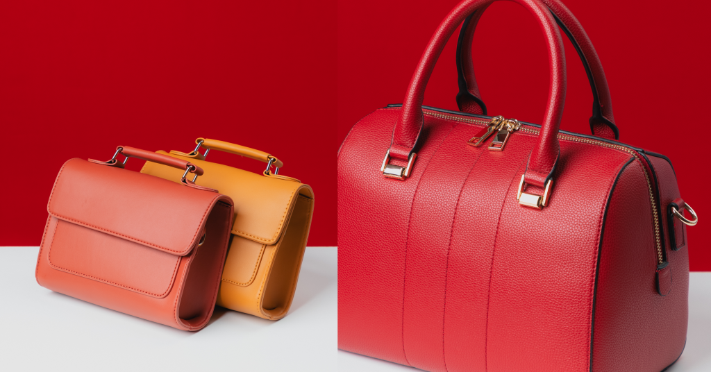 Red and Orange leather bags with two handles, sitting on a wooden table.