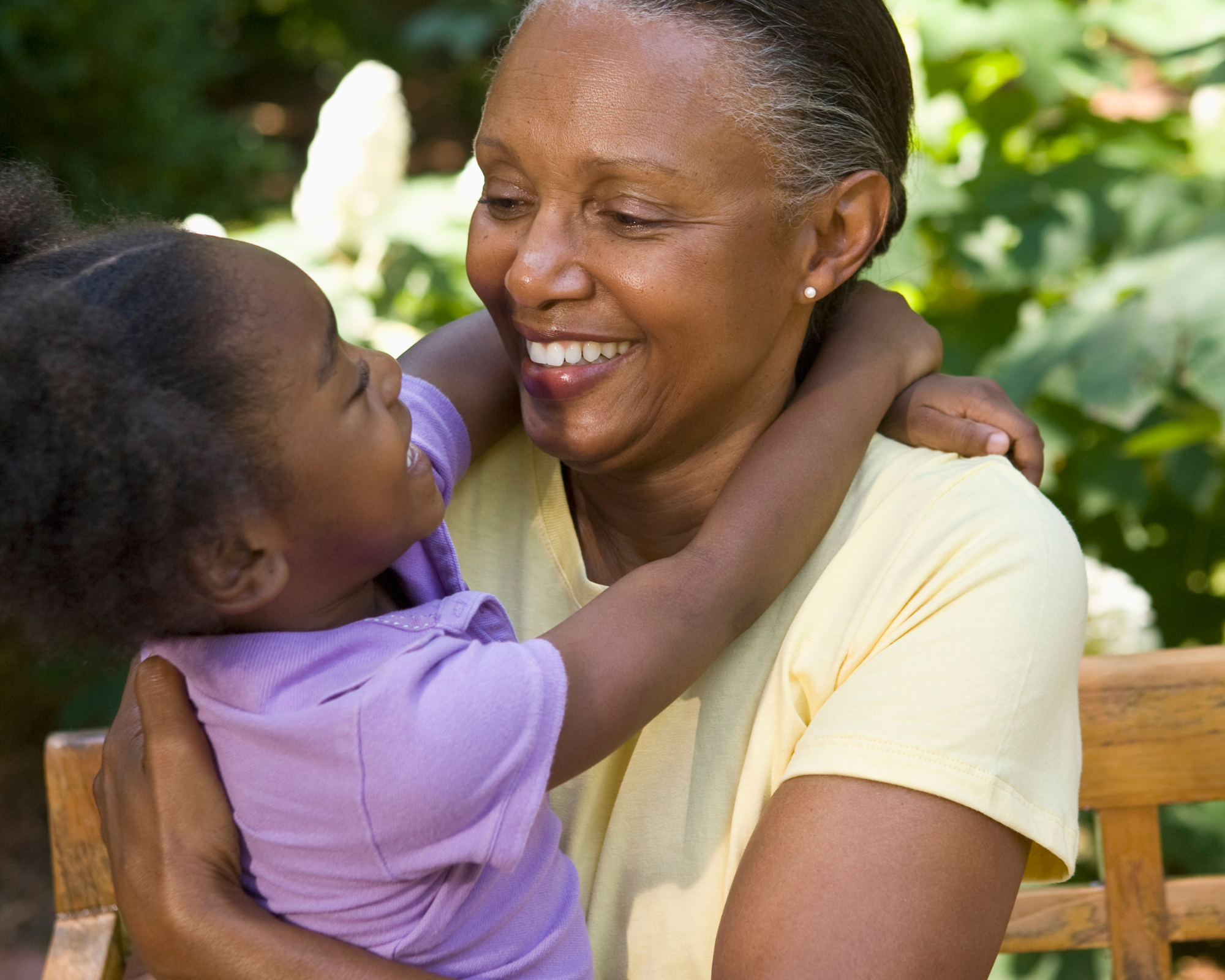 An African Mum wearing a yellow shirt cuddling her grand-daughter in front of a garden